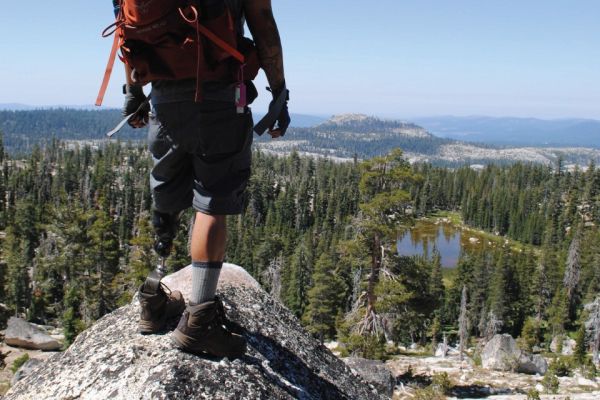 man in shorts standing on a rock peak, hiking in mountains with prosthetic leg