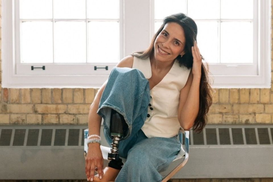 Sonia Montanez seated, smiling with hand on prosthetic foot propped up on chair seat