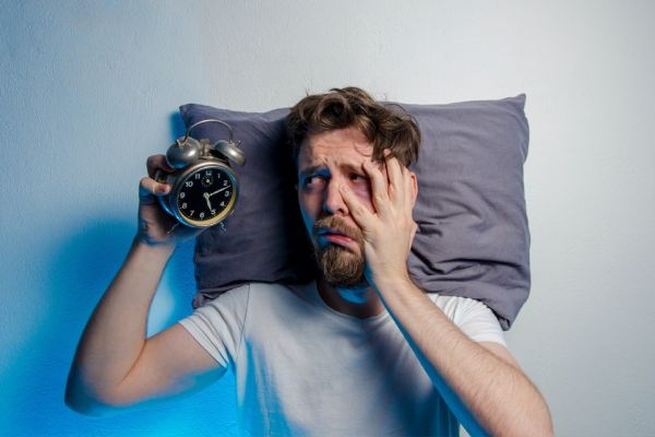Distressed-looking man in bed holding alarm clock in right hand