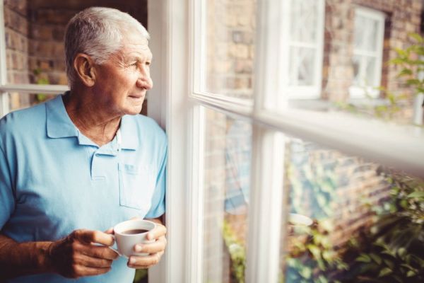 senior white male holding coffee cup looking out window