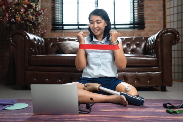 Young leg amputee woman sitting on floor stretching in front of laptop computer