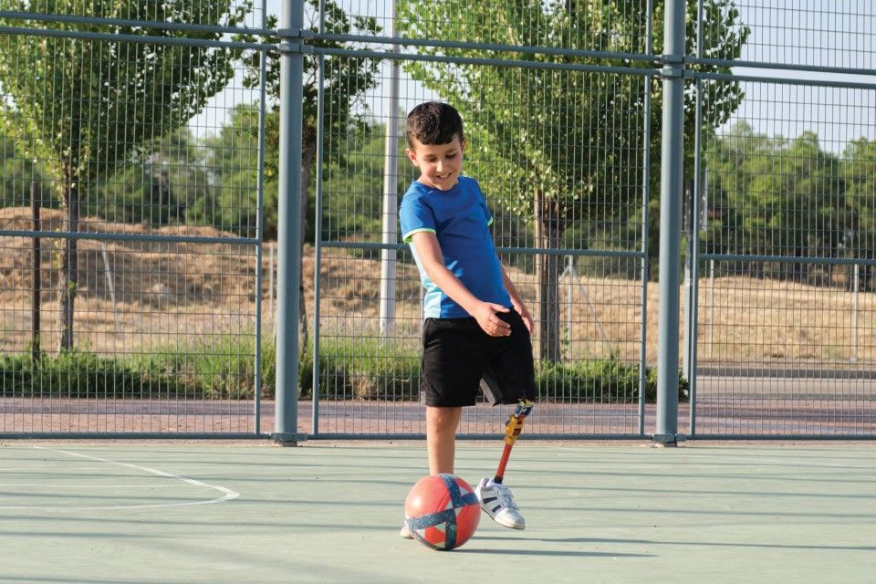 Amputee boy kicking soccer ball on an outside court